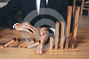 Close up of businessman hand Stopping Falling wooden Dominoes effect from continuous toppled or risk, strategy and successful int