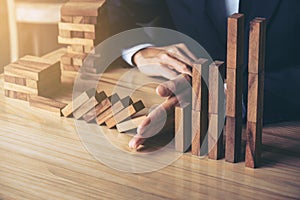 Close up of businessman hand Stopping Falling wooden Dominoes effect from continuous toppled or risk, strategy and successful int