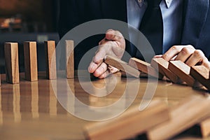 Close up of businessman hand Stopping Falling wooden Dominoes effect from continuous toppled or risk, strategy and successful int