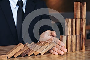 Close up of businessman hand Stopping Falling wooden Dominoes effect from continuous toppled or risk, strategy and successful int