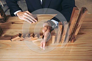 Close up of businessman hand Stopping Falling wooden Dominoes effect from continuous toppled or risk, strategy and successful int