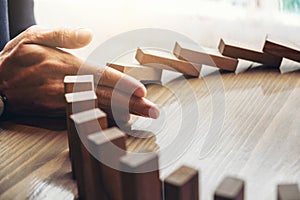 Close up of businessman hand Stopping Falling wooden Dominoes effect from continuous toppled or risk, strategy and successful int