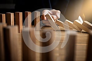 Close up of businessman hand Stopping Falling wooden Dominoes effect from continuous toppled or risk, strategy and successful int