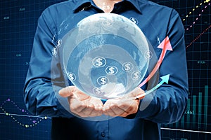 Close up of businessman hands holding glowing globe, financial arrows and money signs on blurry background. Digital world,