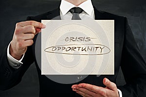 Close up of businessman hands holding paper with creative crisis and opportunity writing on dark wall background. Overcoming