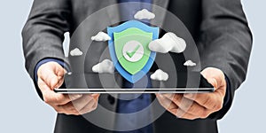 Close up of businessman hands holding tablet with digital shield and clouds on light background. Secure online payment and data