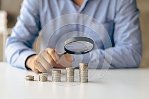 Close up of businessman holding magnifying glass over coins and money