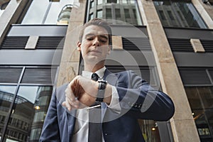 Close up of businessman holding mobile phone in hand and looking at watches.