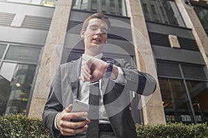 Close up of businessman holding mobile phone in hand and looking at watches.