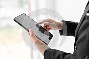 Close up businessman is holding the tablet and pointing his finger on the screen with urban background out of the window. Business