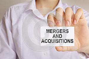 close-up on businessman holding a white paper card with text MERGERS AND ACQUISITIONS, business concept image