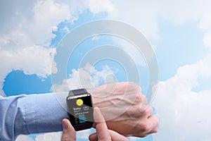 Close-up of a businessman man male checking weather on smartwatch app program on a background of blue sky with white clouds