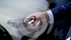 Close-up of businessman pressing car key. Action. Businessman opens car with electronic key and looks at phone. Modern