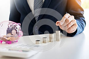 Close up of Businessman putting coin into small piggy bank , The