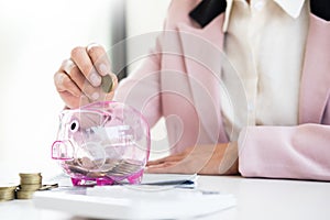 Close up of Businessman putting coin into small piggy bank , The