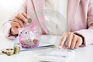 Close up of Businessman putting coin into small piggy bank , The