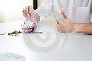 Close up of Businessman putting coin into small piggy bank , The