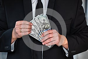 close-up of businessman& x27;s hand in branded suit holding dollar banknotes.