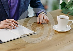 Close-up of businessman`s hand with clock, notepad and cup of aromatic coffee on wooden table