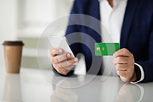 Close-up of a businessman& x27;s hands using a smartphone and holding a green credit card