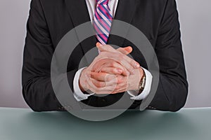 Close up businessman sitting at table with clasped hands.