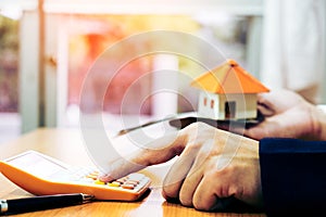 Close-up Of A Businessman Using Calculator Besides House Model In Office