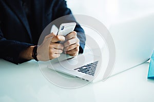 Close up of businessman using mobile phone and laptop computer on desk in modern office