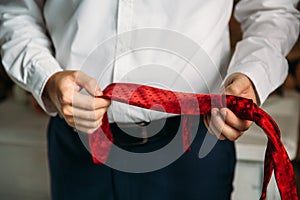 Close-up businessman in white shirt, groom holding red tie in his hands. Concept of men stylish elegance clothes.