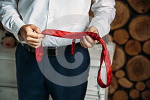 Close-up businessman in white shirt, groom holding red tie in his hands. Concept of men stylish elegance clothes.