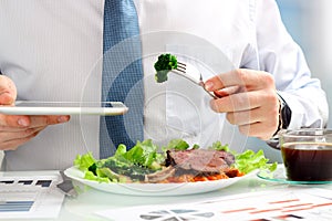 Close-up of businessman working on marketing strategy during business lunch, eating juicy club steak.