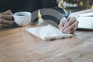 Close up businessman write notebook and and holding coffee cup o