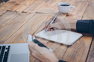 Close up businessman write notebook and using cell phone.