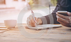 Close up businessman write notebook and using cellphone.