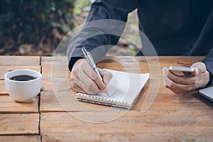 Close up businessman write notebook and using cellphone.