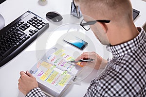 Businessperson With Mobile Phone Writing Schedule