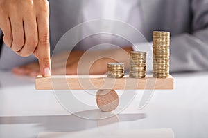 Businessperson Balancing Coins On Wooden Seesaw photo