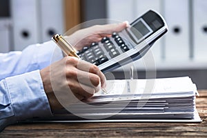 Close-up Of A Businessperson`s Hand Calculating Invoice
