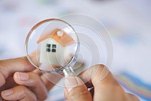 Close-up Of A Businessperson`s Hand Looking At House Model Through Magnifying Glass, House searching concept with a magnifying