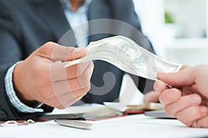 Close-up of businessperson taking bribe from partner on wooden desk. Just hands over the table.