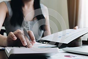 Close-up of businesswoman hand using calculator to calculate business data, accountancy document at home office