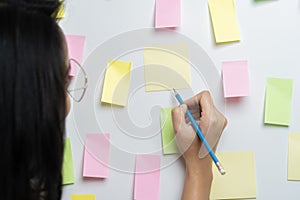 Close-up of businesswoman hand writing on yellow sticky notes stuck over board in creative office