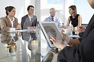 Close Up Of Businesswoman Using Tablet Computer During Board Meeting Around Glass Table