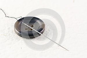 Close up of a button with needle and thread on a white background