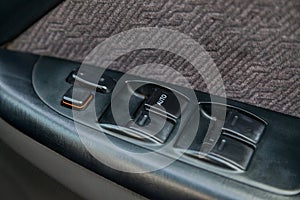 Close-up of buttons for electric adjustment of car windows on a black plastic panel with white signs on the door near the driver