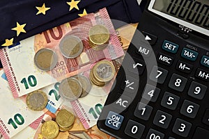 Close-up of a calculator, euro bills and diy facemask, designed as an European Union flag.