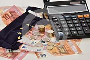 Close-up of a calculator, euro bills and diy facemask, designed as an European Union flag.