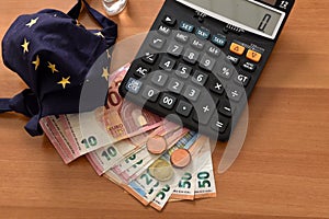 Close-up of a calculator, euro bills and diy facemask, designed as an Europian Union flag.