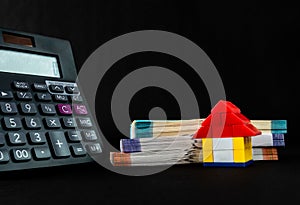 Close up of a calculator, toy home, money bundles shot against black background