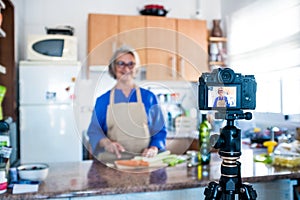Close up of camera filming a mature woman or senior cooking and doing live or video for her social networks and medias -