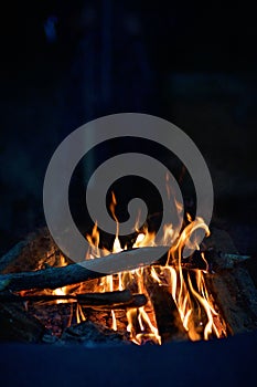 Close-up of a campfire. Fire burning brightly with a big yellow and orange flame in the dark. Firewood and logs burning to ember